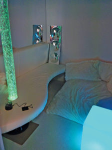 The store’s completed sensory cave contains soothing items for autistic children, including a fiber-optic light, a bubbling LED lamp, a mirror to reflect the light, and a padded floor chair with piles of pillows. The walls lack decoration to keep sensory input to a minimum. (photo courtesy Autism Community Store)