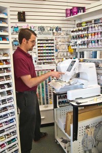 Ross Baldwin demonstrates the features of one of the store’s embroidery machines. (photo by Phil Mumford)